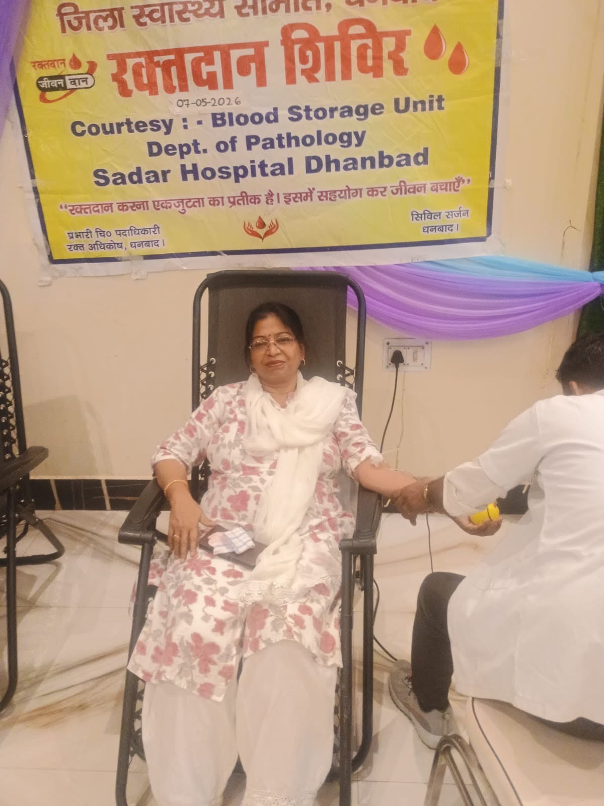 A woman donating blood beneath the Sadar Hospital banner